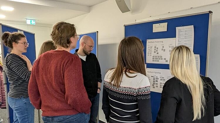 Sechs Personen vor einer Flipchart in einem Konferenzraum.